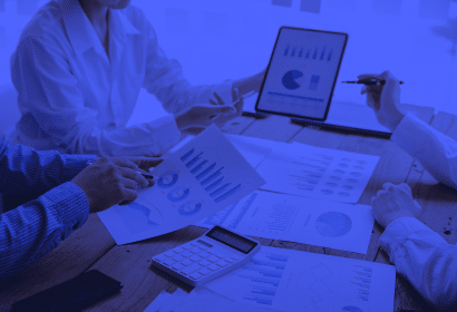 A group of employees in business attire studying charts, doing calculations, and taking notes.