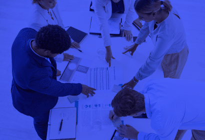 A group of employees in business attire studying charts, doing calculations, and taking notes.